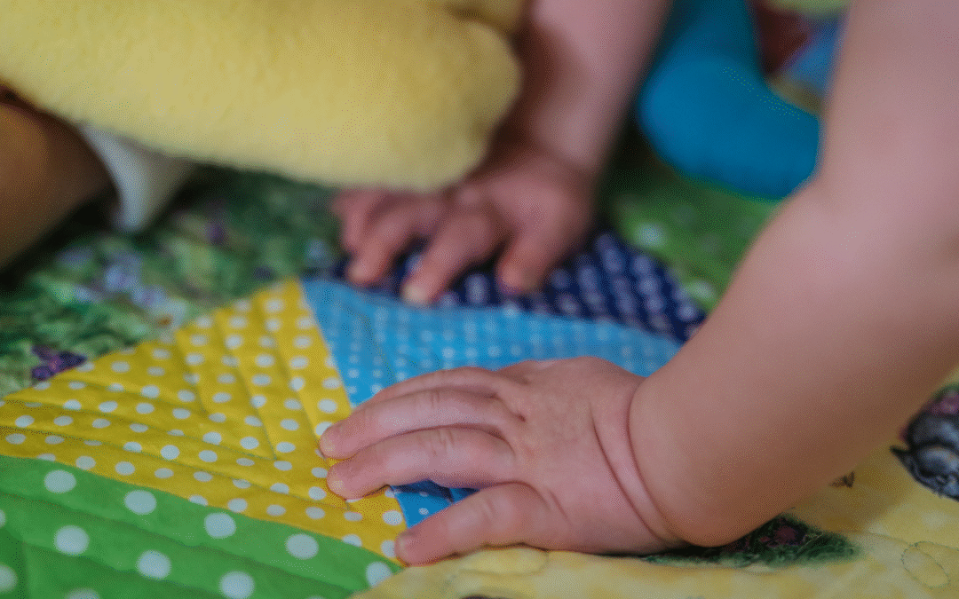The image shows a child's hand on a colourful hand-made quilt