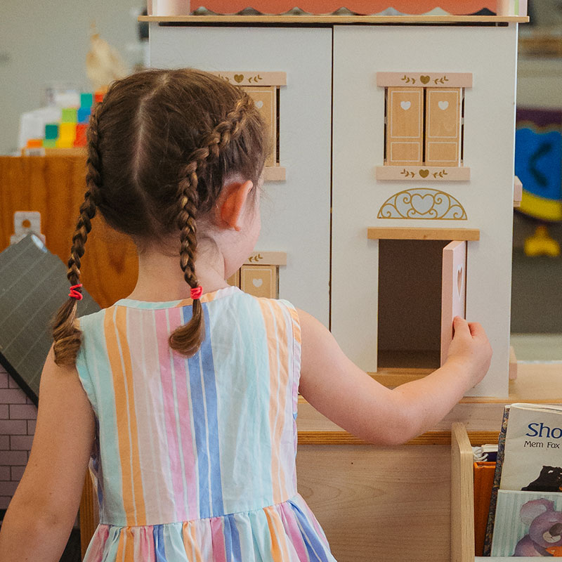 Back view of a young girl opening the door of a dolls house
